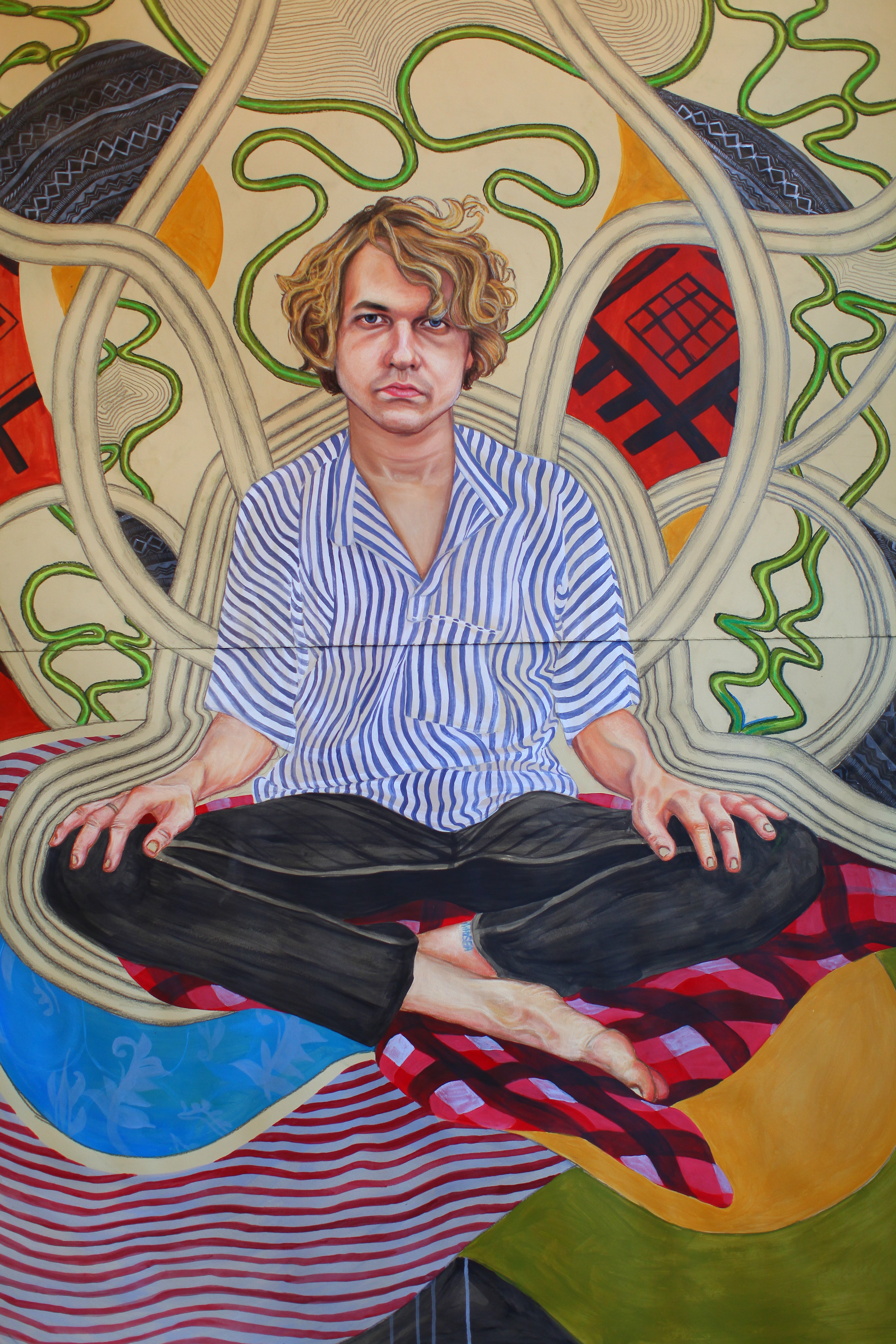 A colorful painted portrait of a seated Kevin Morby with curly hair, wearing a blue-and-white striped shirt and dark pants, surrounded by abstract swirling shapes and patterns in cream, green, red, yellow, and blue. by Artist Maria Calderon